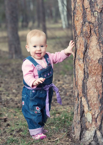Gelukkig babymeisje staat op poten in de buurt van een boom in het park buiten — Stockfoto