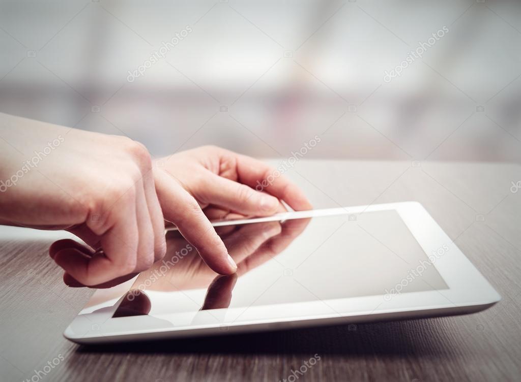 White tablet with a blank screen in the hands on table Stock Photo by