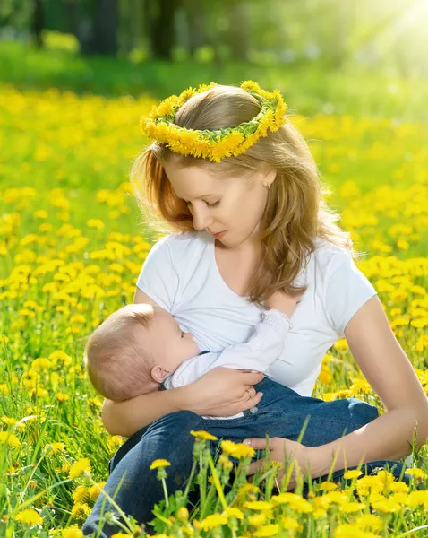 Mãe alimentando seu bebê na natureza prado verde com fluxo amarelo — Fotografia de Stock