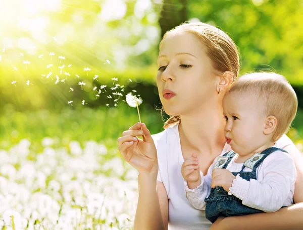 Familia feliz. Madre y niña soplando en una flor de diente de león — Foto de Stock