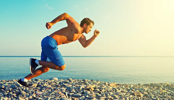 Homme athlète courir au bord de la mer au coucher du soleil en plein air — Photo