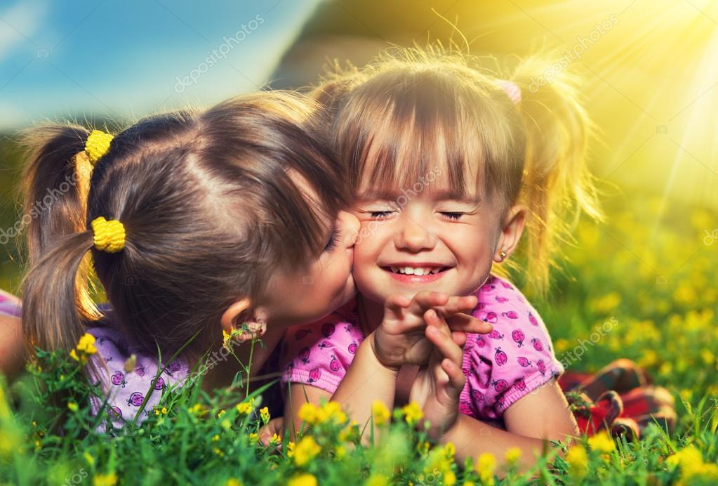 Feliz niñas gemelas hermanas besándose y riendo en el verano outd