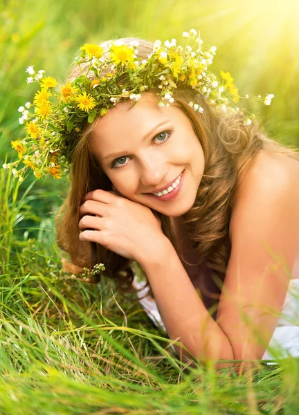 Beautiful woman in wreath of flowers lies in the green grass out — Stock Photo, Image
