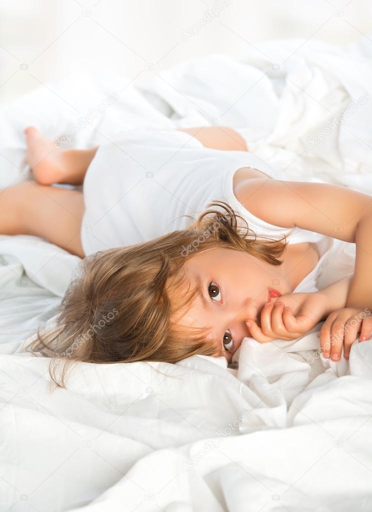 little girl lying in bed and sucks a finger