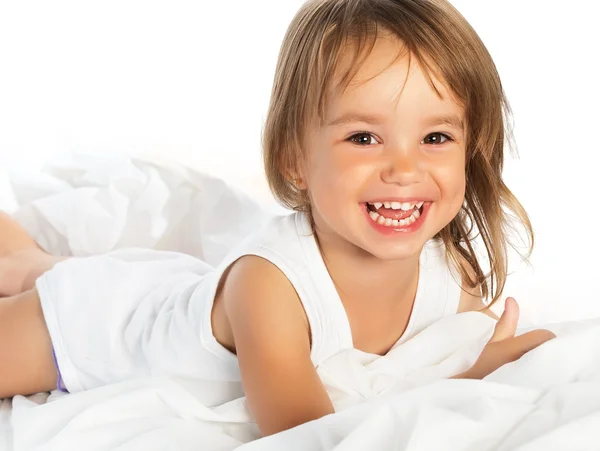 Pequena menina alegre sorridente feliz em uma cama isolada — Fotografia de Stock