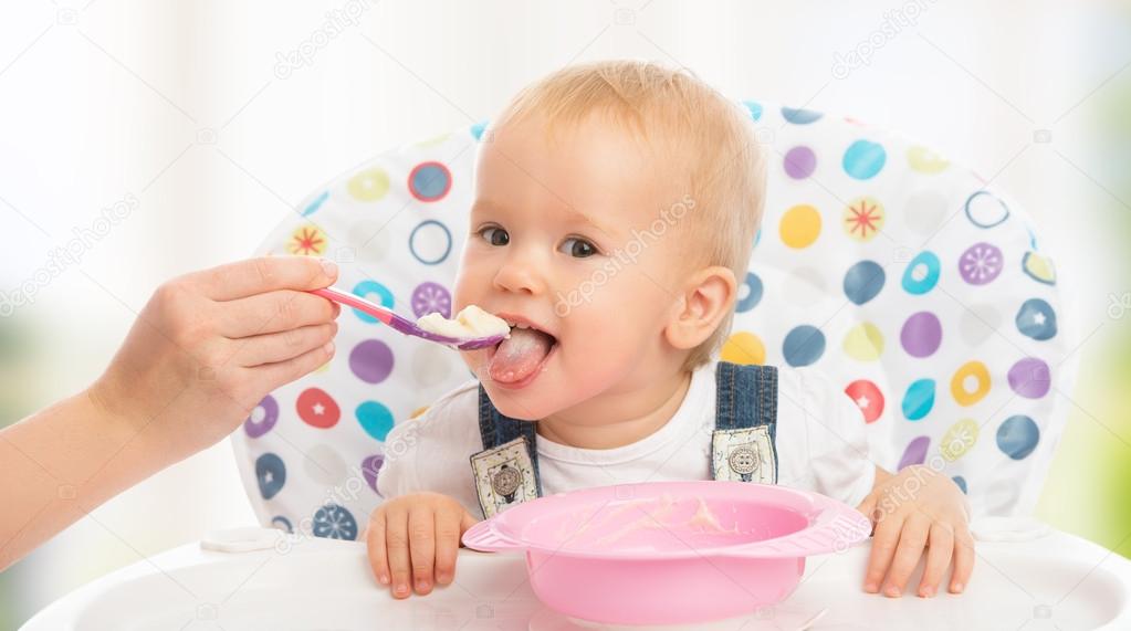 Happy mother feeds funny baby from spoon