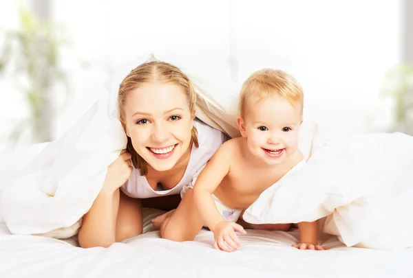 Família feliz mãe e bebê sob cobertores na cama — Fotografia de Stock