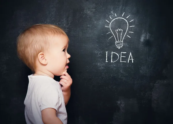 Baby child at the blackboard with chalk drawn bulb symbol ideas — Stock Photo, Image