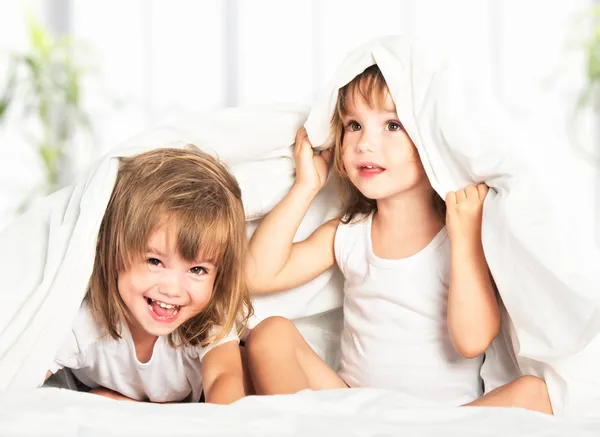 Happy little girls twins sister in bed under the blanket having — Stock Image Happy little girls twins sister in bed under the blanket having Stock Photo