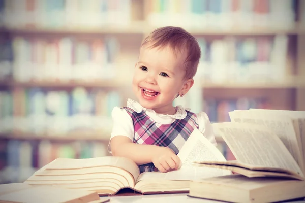 Happy baby girl reading a book in a library — Stock Photo, Image