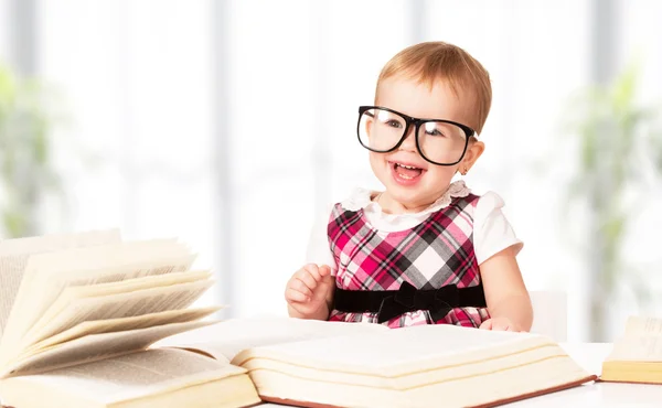 Lustiges kleines Mädchen mit Brille liest ein Buch in einer Bibliothek — Stockfoto