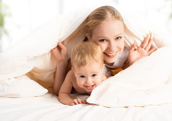 Feliz familia madre y bebé bajo mantas en la cama — Foto de Stock