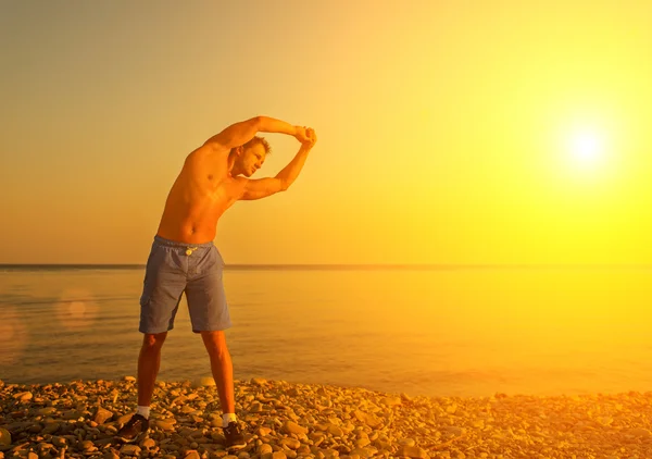 Спортсмен практикующий, занимающийся спортом и йогой на пляже на солнце — стоковое фото