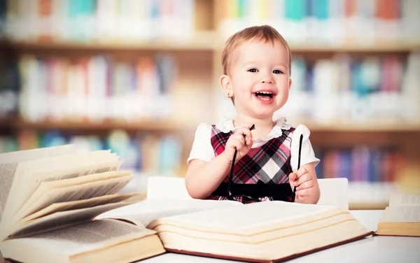 Lustiges kleines Mädchen mit Brille liest ein Buch in einer Bibliothek — Stockfoto