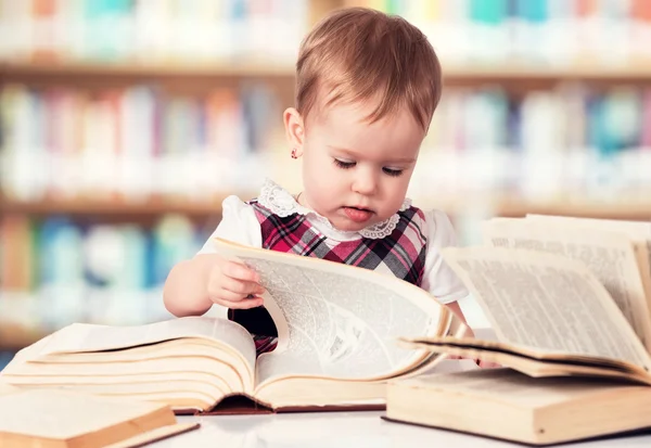 Glad flicka som läser en bok i ett bibliotek — Stockfoto