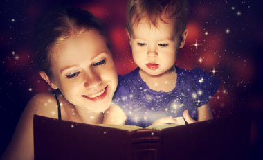 Anne ve çocuk bebek kızı sihirli kitap okumak içinde karanlık