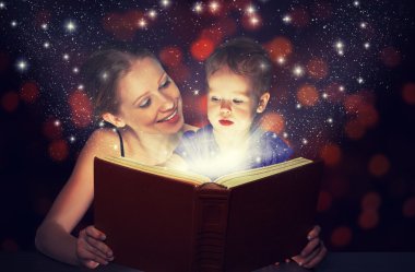 Anne ve çocuk bebek kızı sihirli kitap okumak içinde karanlık