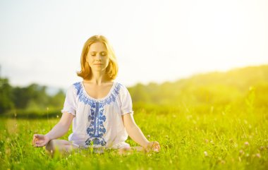 Yeşil çimenlerin üzerinde yoga yaparken genç bir kadın