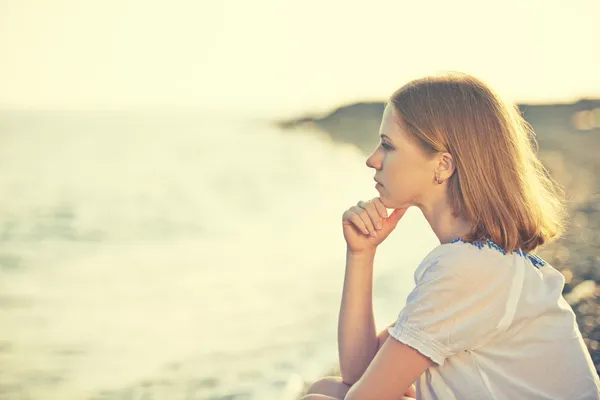 Triste chica sentada en la playa y mira a la distancia en sí — Foto de Stock