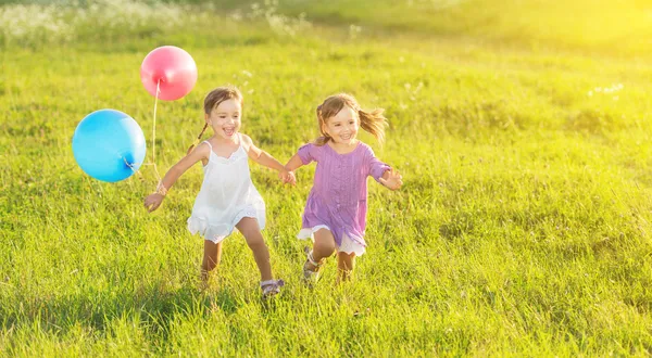 Glückliche Zwillingsschwestern laufen im Sommer lachend herum und spielen mit Luftballons — Stockfoto