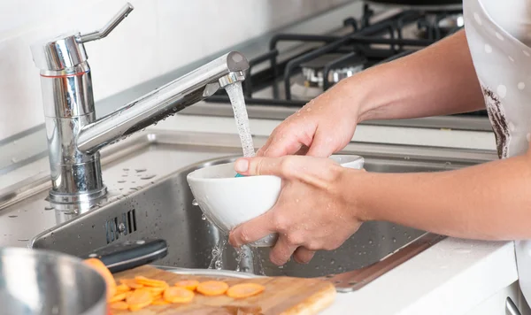 Mujer lavar los platos bajo un grifo corriente —  Fotos de Stock