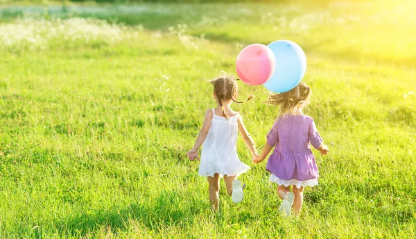 Niñas felices hermanas gemelas con globos en el campo de verano en la naturaleza —  Fotos de Stock