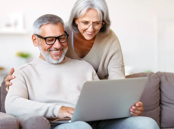 Feliz pareja de ancianos de la familia viendo la comedia o el vídeo divertido en el ordenador portátil, mientras que pasar tiempo libre en casa — Foto de Stock