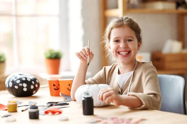 Sevimli küçük kız gülümsüyor, elinde boya fırçası ve evde Cadılar Bayramı balkabağı resmi tutuyor. — Stok fotoğraf