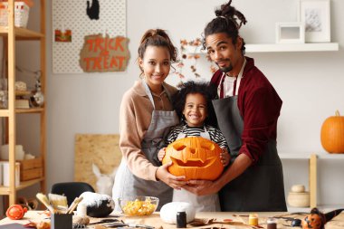 Mutlu aile, anne, baba ve oğul Jack O Fener yaparken kameraya gülümsüyor.