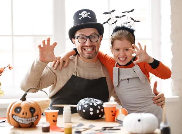 Glücklich lächelnde Väter und Töchter mit Halloween-Hüten, die in die Kamera lächeln und gruselige Gesten machen, während sie Hausdekorationen vorbereiten — Stockfoto