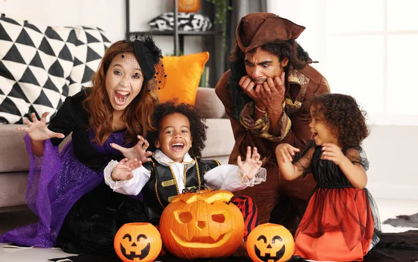 Familia afroamericana en disfraces de Halloween haciendo gesto de miedo mientras se sienta con Jack o linterna —  Fotos de Stock