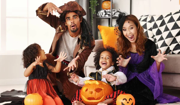Familia afroamericana en disfraces de Halloween haciendo gesto de miedo mientras se sienta con Jack o linterna —  Fotos de Stock
