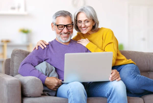 Beautiful mature family couple looking at laptop with smile on face while spending time together — Stock Photo, Image