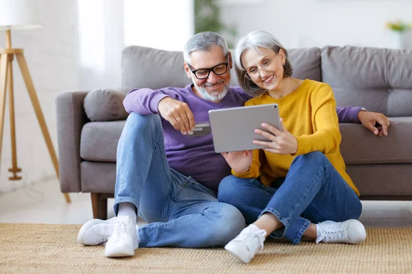 Beautiful mature family couple looking at tablet with smile on face while spending time together — Stock Photo, Image