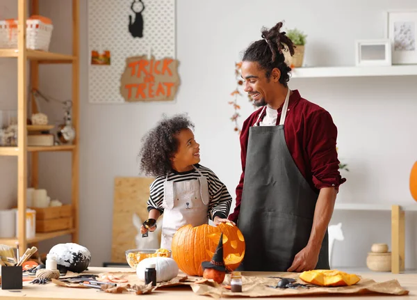 Şirin, mutlu küçük Afrikalı Amerikalı çocuk evde babasıyla Cadılar Bayramı balkabağı oyuyor. — Stok fotoğraf