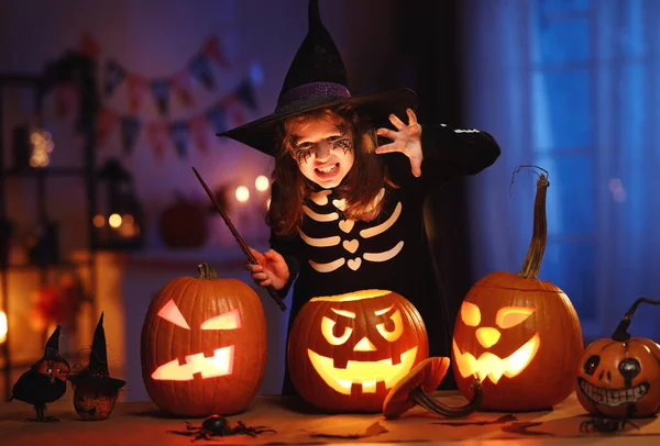 Petite fille en chapeau de sorcière et costume de squelette avec baguette magique à la main avec visage effrayant — Photo