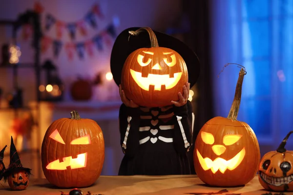 Menina em traje de Halloween segurando brilhante jack-o-lanterna esculpida abóbora na frente da cara — Fotografia de Stock