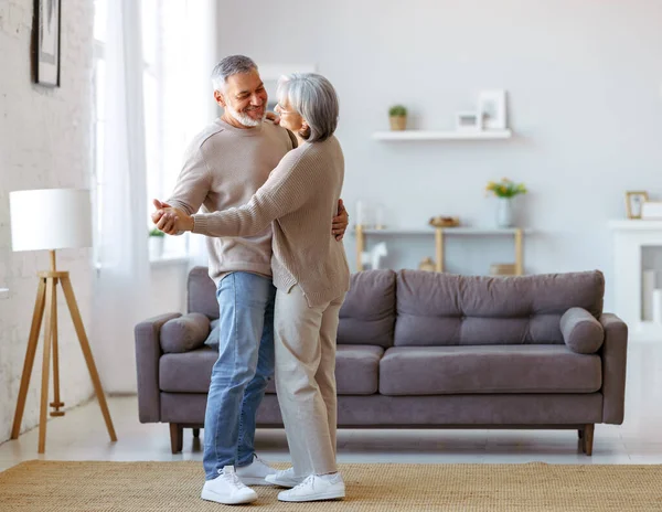 Glad senior par kär tittar på varandra med ömhet, dansar tillsammans i vardagsrummet Royaltyfria Stockbilder