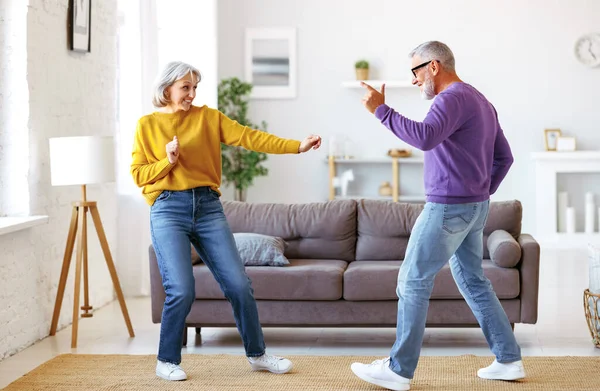Energetický starší rodinný pár tančí společně v obývacím pokoji doma, stěhuje se k hudbě Stock Obrázky