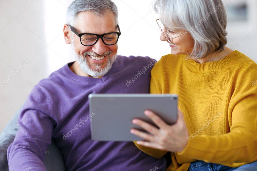Beautiful mature family couple looking at tablet with smile on face while spending time together