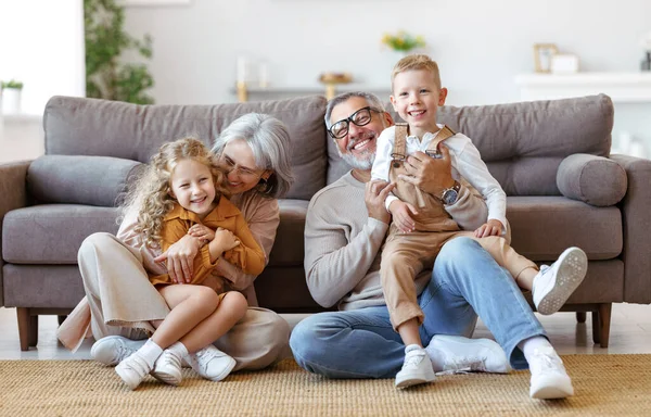 Boldog család nagyszülei és két kisgyerek ölelkeznek és mosolyognak a kamera előtt, miközben a padlón ülnek. — Stock Fotó