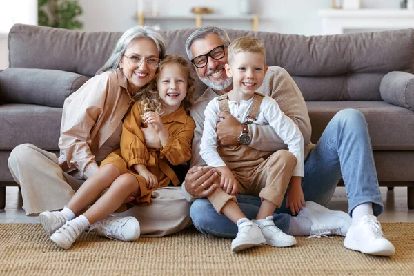 Glückliche Familiengroßeltern und zwei kleine Kinder umarmen und lächeln in die Kamera, während sie auf dem Boden sitzen — Stockfoto