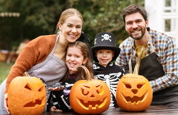 Boldog fiatal család Halloween jelmezek faragás tök együtt a kertben — Stock Fotó