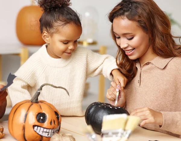 Linda niña afroamericana pintando calabaza de Halloween con mamá juntos en casa —  Fotos de Stock