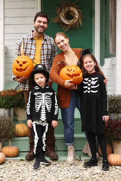 Junge glückliche Familieneltern mit Kindern stehen während der Halloween-Feiertage auf der Veranda des Hauses — Stockfoto