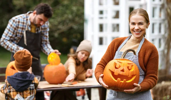 Donna sorridente con jack-o-lanterna che sorride alla macchina fotografica mentre intaglia zucche con la famiglia nel cortile — Foto Stock