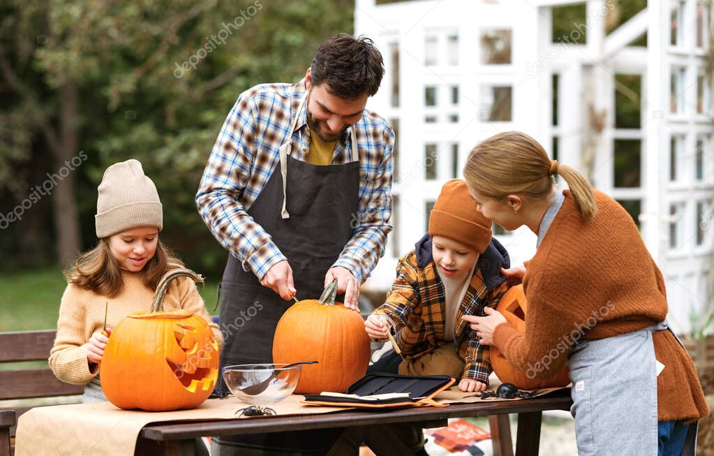 Happy young family carving pumpkins in backyard, children making jack-o-lantern with parents