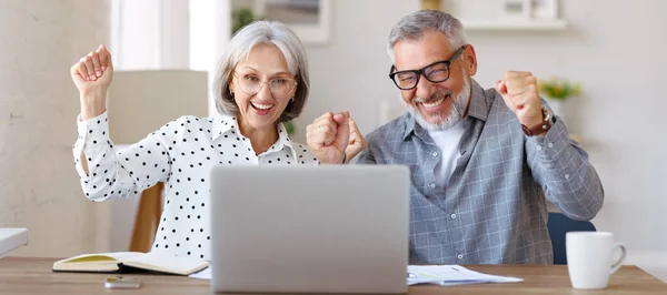 Ευτυχισμένο ζευγάρι ηλικιωμένων γιορτάζει την επιτυχία, ενώ κάθεται στο τραπέζι με ανοιχτό φορητό υπολογιστή στο σπίτι — Φωτογραφία Αρχείου