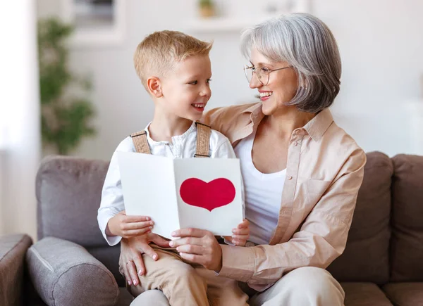 Carino nipotino ragazzo congratulandosi con la nonna sorridente e dando biglietto di auguri fatto a mano — Foto Stock