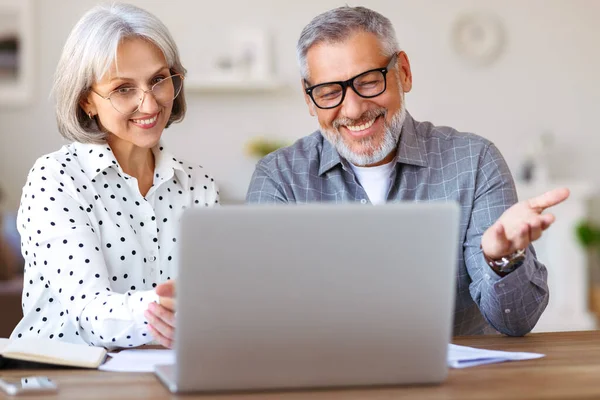 Senior familj par studerar online tillsammans hemma, titta på bärbar dator när du sitter vid bordet — Stockfoto